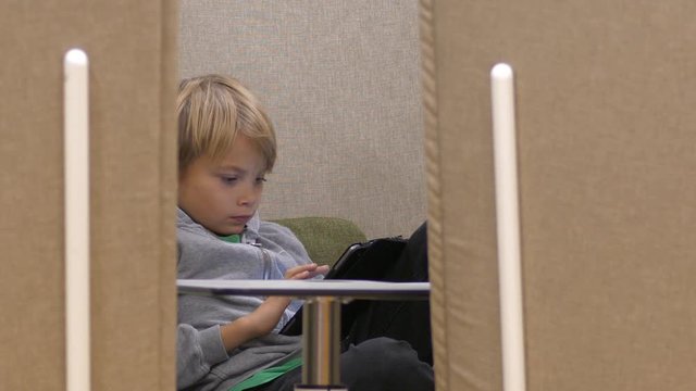 School boy studying on a tablet seen through a gap of cozy sofas, Static