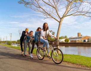 Four teens having fun outdoors, beside a river, with roller skates and a bicycle