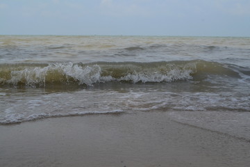 Brown-ish sea waves beside seashore, sand captured in daytime.