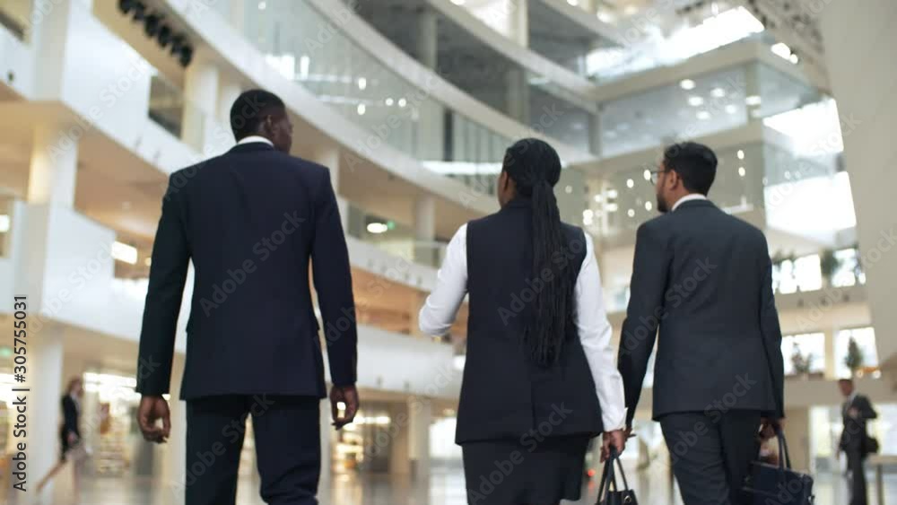 Poster rear view of three business partners of different ethnicities walking to office and discussing desig