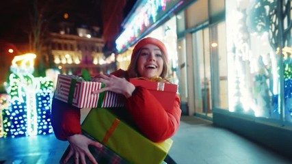 Cheerful young woman running in the street falling Christmas boxes presents on the ground. Busy female customer in hurry delivering holiday gifts in beautiful winter evening city. - Powered by Adobe