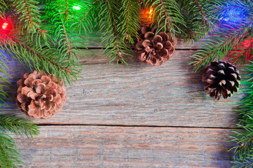 Christmas tree branches, pine cones and illuminated garlands on wooden background, top view with copy space