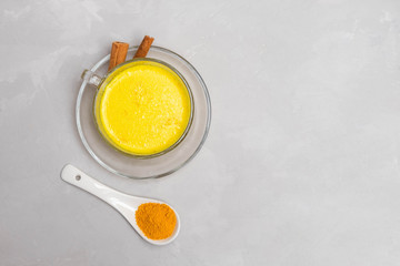 Obraz na płótnie Canvas Anti-Inflammatory Turmeric golden milk in a glass cup with cinnamon sticks and turmeric powder on grey concrete table