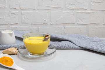 Hot healthy drink turmeric golden milk with turmeric powder, ginger root, milk, cinnamon stick on grey concrete table