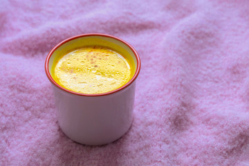 Mug of warm healthy drink turmeric golden milk on soft pink knitted background.