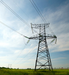 Electrical net of poles on a panorama of blue sky and green meadow