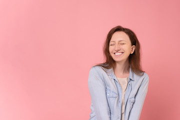 Fototapeta premium Laughing cheerful positive young woman in casual wear posing on a pink background. Happy young millennial girl rejoices at discounts and promotions in the store. Advertising space