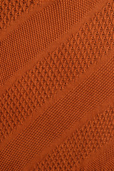 Orange knitted plaid closeup. Knitted texture with diagonal ornament. Detailed warm background made of yarn. Natural woolen fabric, fragment of a sweater for design. Copy space. View from above