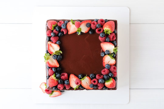 Square Cake On Birthday Decorated With Fresh Berries, Poured With Chocolate On A White Background. Top View.