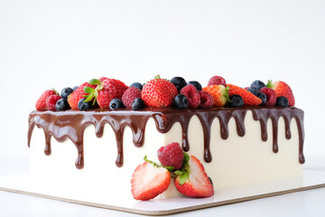 Square cake on birthday decorated with fresh berries, poured with chocolate on a white background.