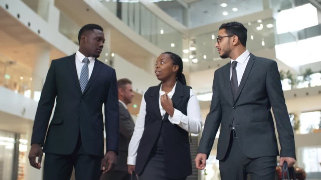 Group of three multiethnic businesspeople, two men and one woman, walking to work and discussing project, front view medium shot