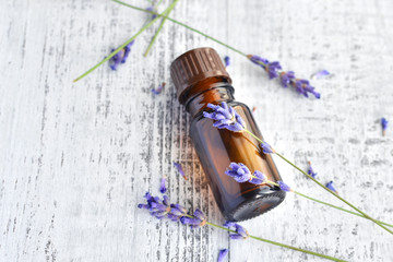Organic herbal oil in dark glass bottle and fresh lavender flowers on old wooden table background
