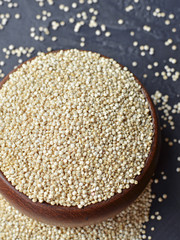 Uncooked organic quinoa grains in wooden bowl on dark background. Cooking ingredients, super food.
