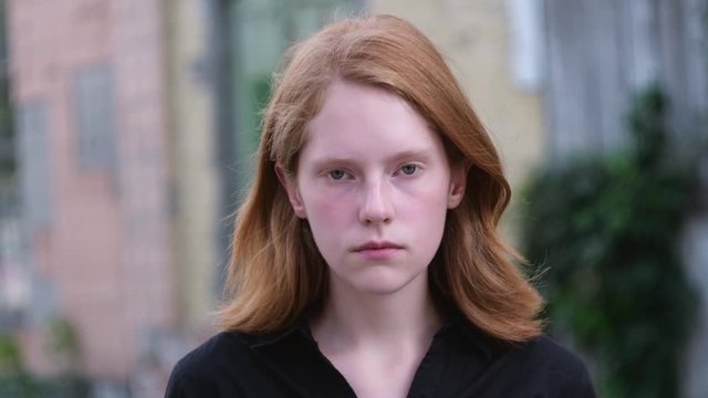 Child loneliness. Sad ginger girl orphan thought. Homeless redhead child is depressed outside the abandoned building.