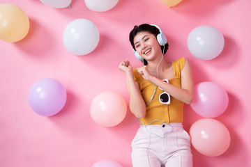 Asian Beauty girl with colorful air balloons laughing over pink background. Young woman on birthday holiday party. Celebrating with pastel color balloon.She listen music and dance.