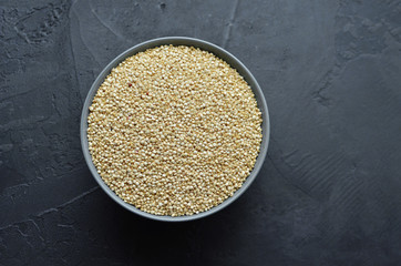 Dry organic quinoa seeds in gray ceramic bowl on dark concrete background