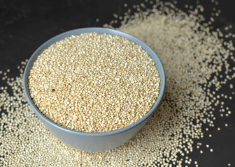 Bowl with raw white uncooked quinoa seeds on dark concrete background