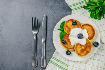 Pancakes with fresh blueberries, mint and sour cream on white plate. Healthy breakfast food. Table top view. Grey background