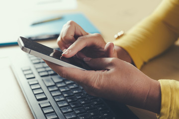 Female holding smartphone getting message with confirmation making transaction on laptop computer.
