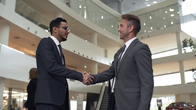 Two businessmen in suits and neckties shaking hands to greet each other in business center