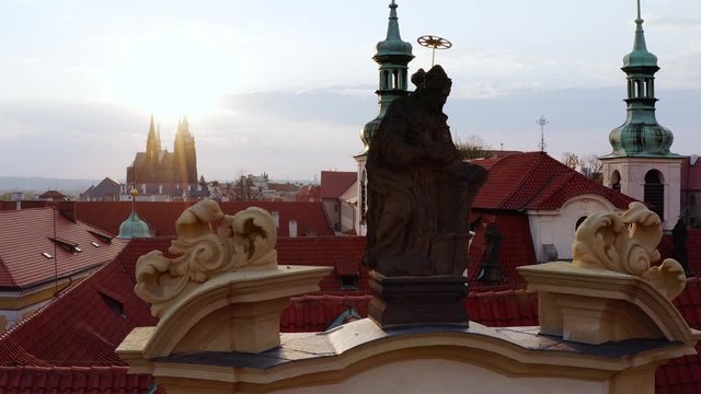 Top view statue on facade of historic cathedral. Lateral movement, drone flying near sculpture of saint in shining decorating facade famous Lareta church over roofs and belfry in old town of Prague