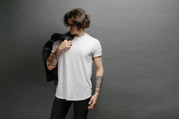 Hipster handsome male model with glasses wearing white blank t-shirt and black jeans with space for your logo or design in casual urban style - obrazy, fototapety, plakaty