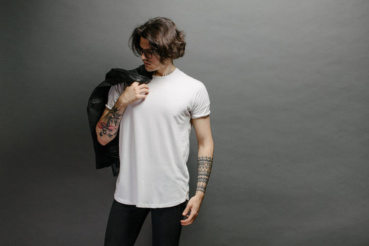 Hipster handsome male model with glasses wearing white blank t-shirt and black jeans with space for your logo or design in casual urban style