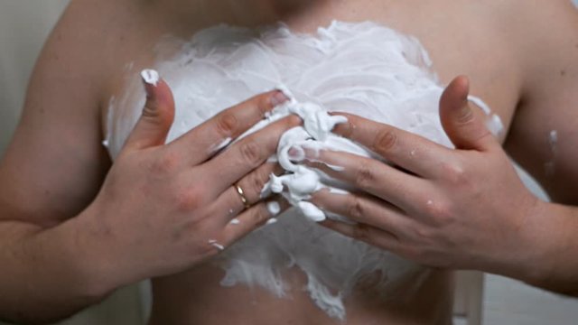 Shirtless young man putting shaving foam on his palm while preparing to shave his chest. Breast hair removal in men