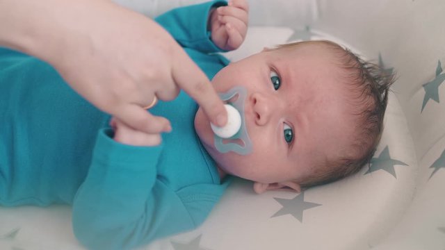 young mother gives dummy to upset crying little baby in cozy cocoon with stars in light room closeup