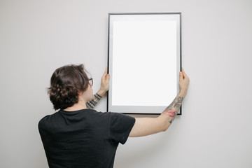Man hanging a picture or a poster for mock up on a wall wearing black clothes