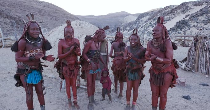 4K view of Himba woman in traditional dress dancing and singing outside their clay hut, Namibia