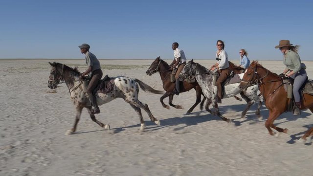 Slow motion view of a group of horse riders having fun galloping across the wide open spaces of the Makgadikgadi salt Pans 