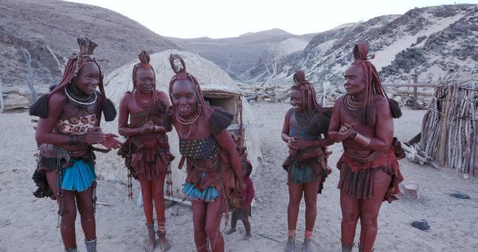 4K view of Himba woman in traditional dress dancing and singing outside their clay hut, Namibia