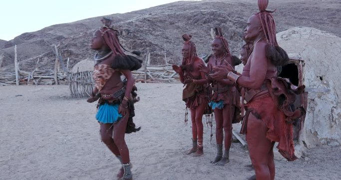 4K view of Himba woman in traditional dress dancing and singing outside their clay hut, Namibia