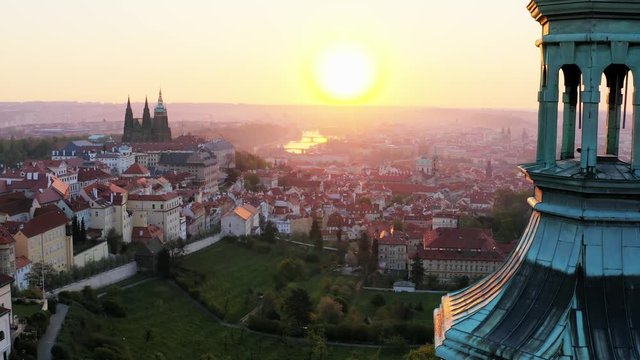 Aerial view cropped steeple of Strahov monastery at sunrise. Sun shining through belfry camera moving near towers of ancient cathedral , showing picturesque panorama above history centre of Prague 