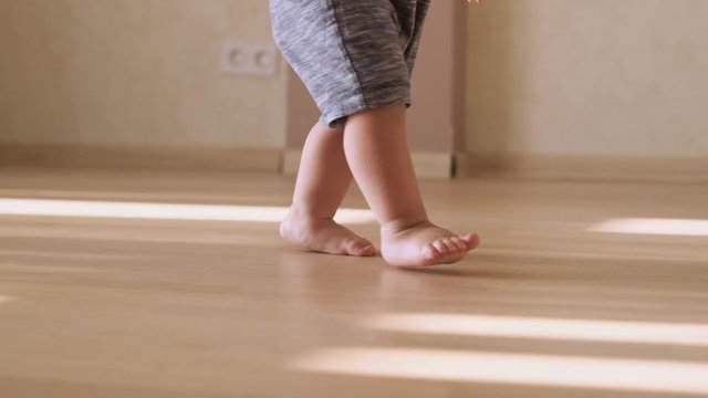 Little feet walking on floor, close-up. Baby learning to walk at home. Baby first steps. Slow motion