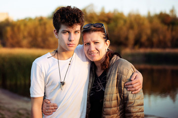 A teenage boy embraces his mom with great love and tenderness. Mom and son walking in the park together to talk