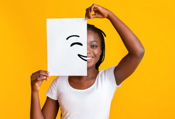 Black woman covering half face with smiley picture