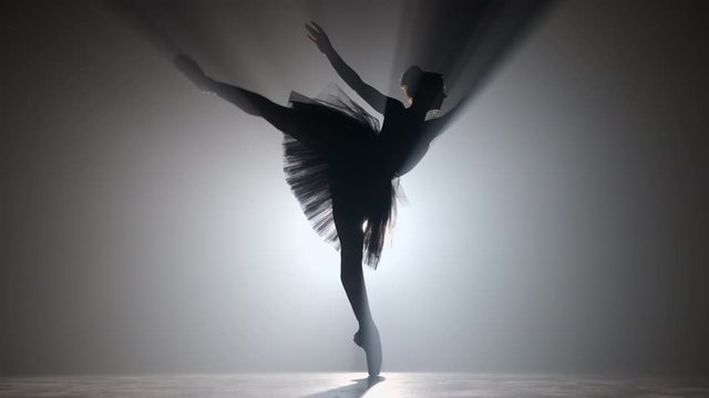 Professional ballerina dancing ballet in spotlights smoke on big stage. Beautiful young girl wearing black tutu dress on floodlights background. Black and white. 4k