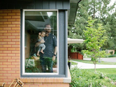 Father Holding His Daughter Behind Window Of House