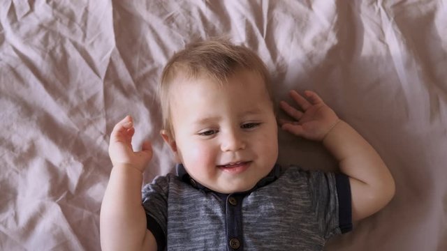 Top view of baby looking at camera and smiling, close up sloe motion. A cute little baby is look and smile. Babyboy looks around and smiles and laughs, view drom above