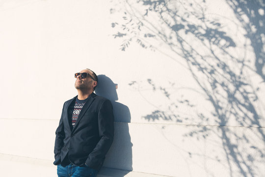 Man wearing sunglasses and blazer by white wall