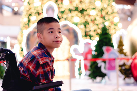 Disabled Child On Wheelchair With Blurry Lights And Decorations On The Christmas Tree, Special Children's Lifestyle, Life In The Education Age Of Special Need Kids, Happy Disability Kid Concept.