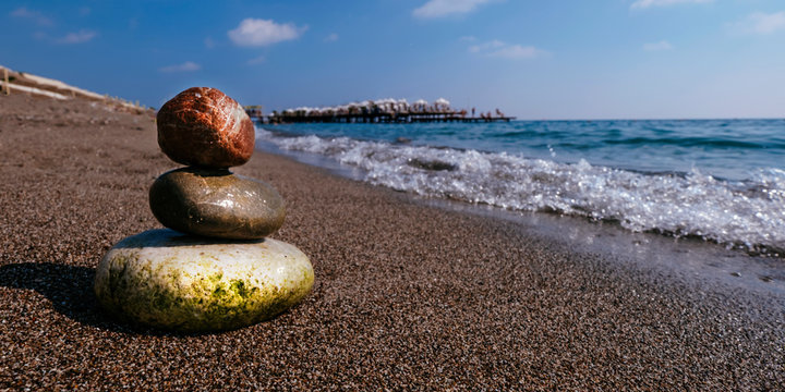 Stack of zen stones on beach near sea. Tower of spa rocks on sand at ocean. Balanced pebbles outdoors on sunny summer day. Oriental calm and harmony symbol. Wellness and tranquility concept