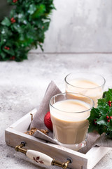 Winter spicy hot drink eggnog in a glasses with cinamon in stone plate, ice frost branches on light stone table