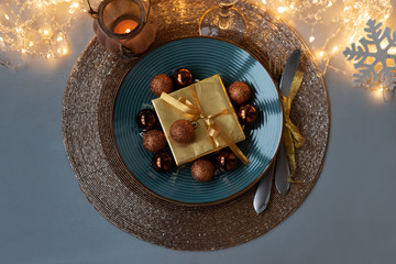 Top view on Christmas table setting. Golden decoration with gift box, glass baubles and defocused lights. Christmas and New Year holidays concept. Flat lay.