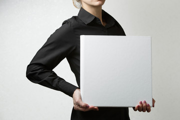 woman holds square family photo book with copy space for text. person looks at  photobook. sample  white photo album in palms close up portrait on background . wedding photoalbum with  leather cover.