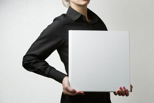 woman holds square family photo book with copy space for text. person looks at  photobook. sample  white photo album in palms close up portrait on background . wedding photoalbum with  leather cover. - Powered by Adobe