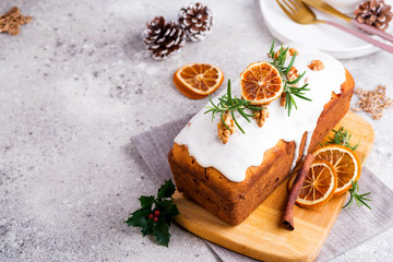 Fruit loaf cake dusted with icing, nuts and dry orange on stone background. Christmas and Winter Holidays