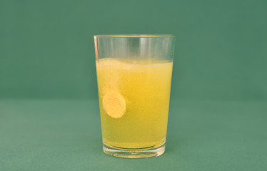 The effervescent tablet dissolves in a glass of water isolated on the green background